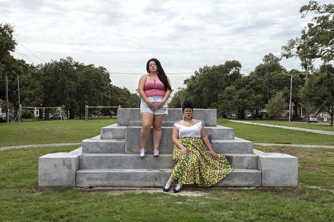 Photograph entitled The Rise and Fall Take Em Down by Genevieve Gaignard. The artist appears twice in the image with different clothing. One stands on the industrial cement structure as the other sits