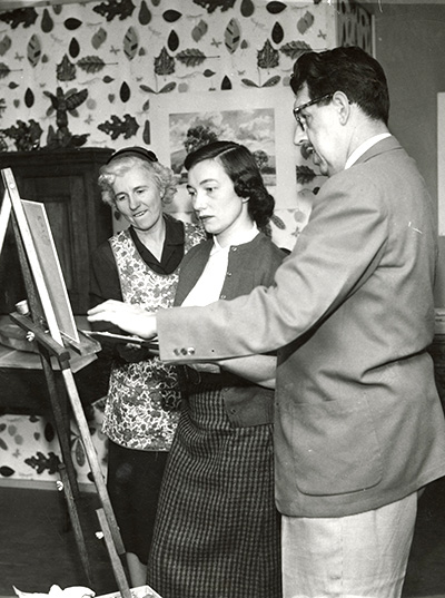 Old photo of student being instructed on a painting from professors
