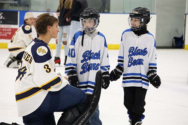 An MCLA hockey player speaks with kids in hockey gear