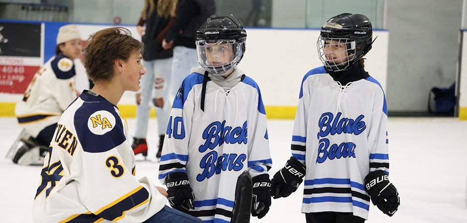 An MCLA hockey player speaks with kids in hockey gear