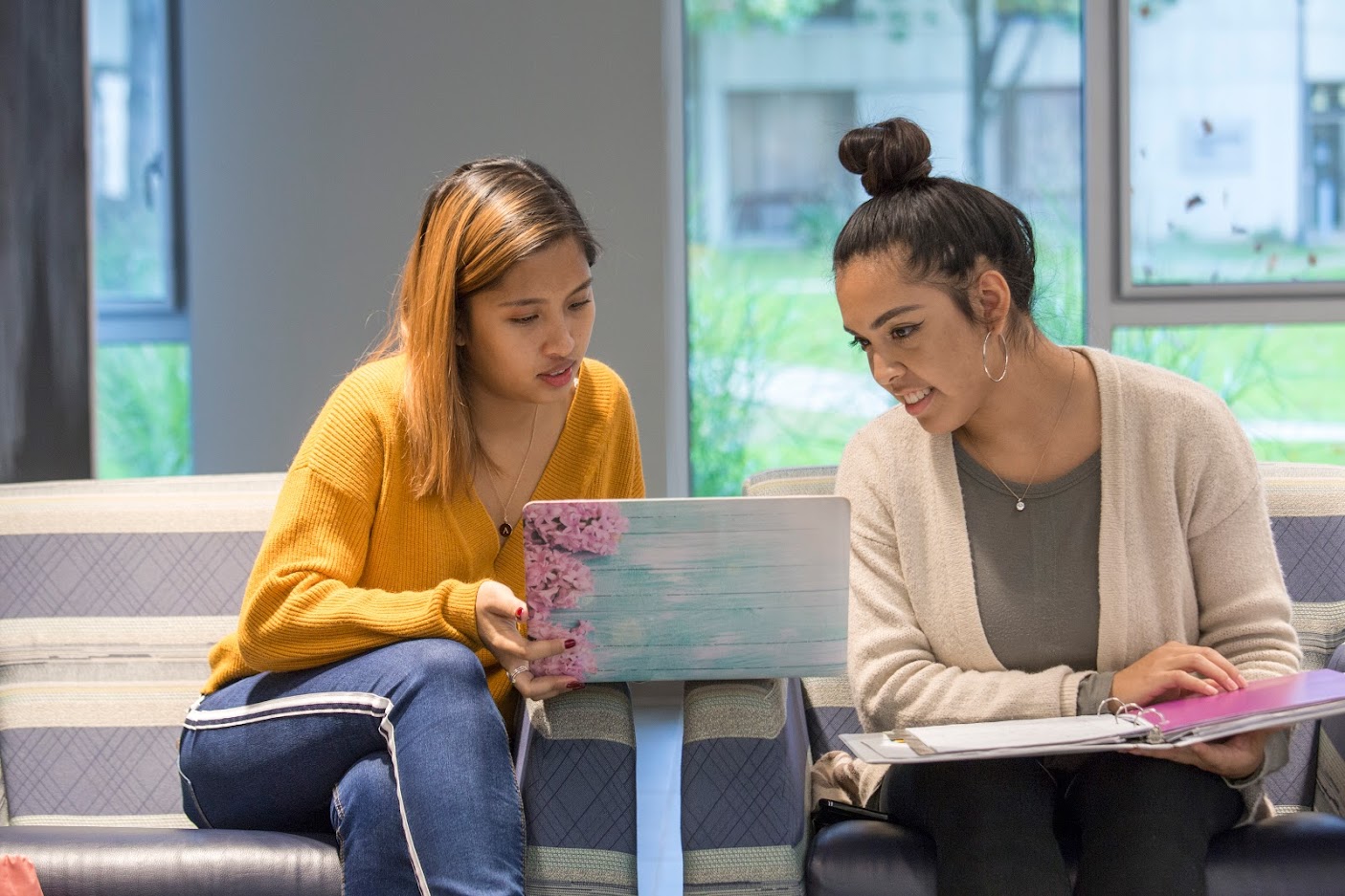Students sitting side by side looking at a laptop together with a notebook open 
